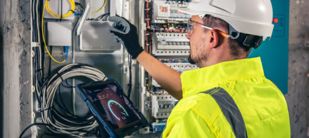 Man Electrical Technician Working Switchboard with Fuses Uses Tablet - LC Electrical Services